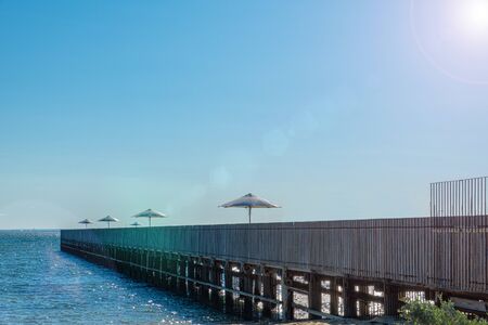Long wooden pier with large sun shade umbrellas under bright sunlight in diminishing perspective - vacation conceptの写真素材
