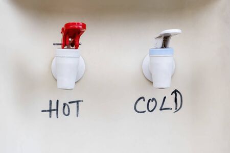 Hot and cold drinking water dispenser taps closeup with hand writing