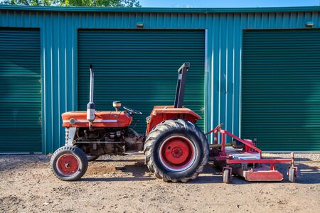 Old tractor with attached lawn mower against warehouse doors in Australia