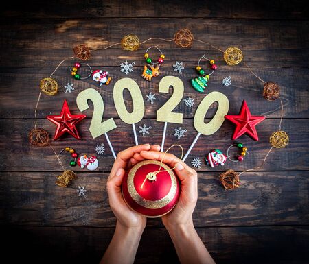 Happy new year 2020 concept with Christmas decorations and female hands holding bauble against wooden backgroundの写真素材