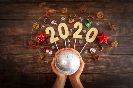 New year 2020 concept with Christmas decorations and female hands holding silver bauble against wooden background - top viewの写真素材