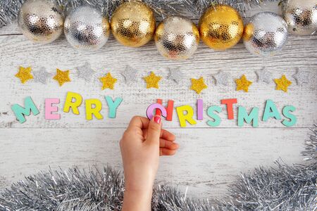 Girls hand placing the letter C into the Merry Christmas text on the table with baubles and tinselの写真素材