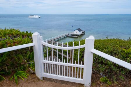 White wooden gate leading to pier with passenger ferry crossing the bay in the distanceの写真素材