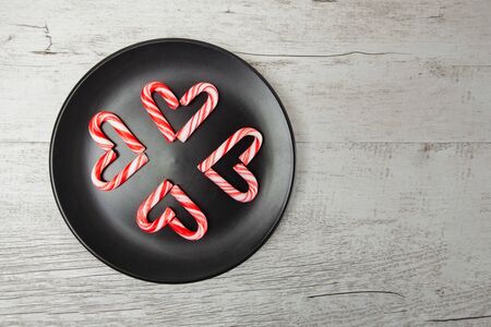 Candy canes arranged in heart shapes on black plate and white wooden background with copy spaceの写真素材