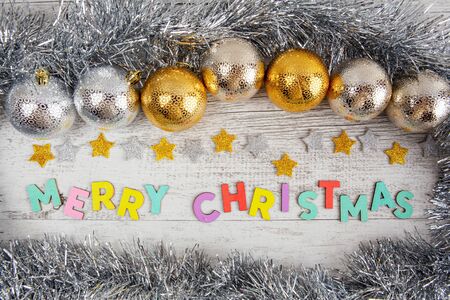 Merry Christmas colorful text on white wood with golden silver baubles and tinselの写真素材