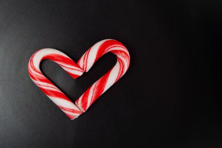 Candy canes arranged in heart shape on black background with copy spaceの写真素材