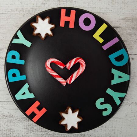 Happy Holidays colorful text on black plate with candy canes in heart shape - top viewの写真素材