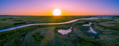 Scenic river flowing among meadows and pastures at sunset - wide aerial panorama