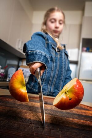 Caucasian girl cutting red apple in half at home in the kitchen. Shallow focus.