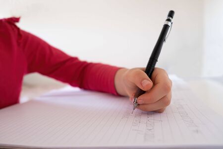 Caucasian child hand writing with mechanical pencil in notebook with shallow focusの写真素材