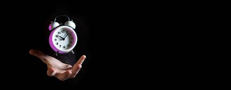 White alarm clock with purple highlights hovering above male hand against black background - narrow...