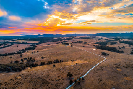 Rural dirt road passing through pastures towards hills silhouettes at sunset - aerial viewの写真素材