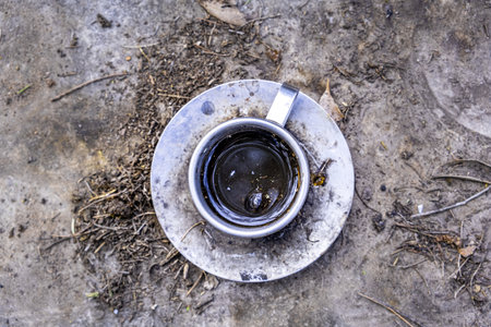 Old decaying metal cup and saucer with dirty coffee leftovers on the groundの写真素材