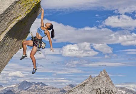 Female rock climber struggles to reach her next grip as she battles her way up a steep cliff.の写真素材