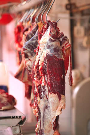 uncooked meat hanging on hooks on open marketの写真素材