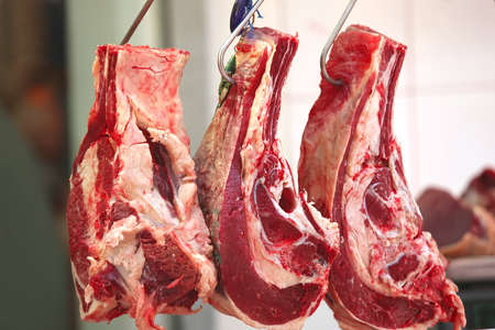 uncooked meat hanging on hooks in show windowの写真素材