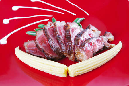 meat served with beans and corns on red plateの写真素材