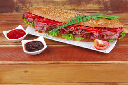 sandwich on plate : french baguette with smoked sausage on white plate over wooden tableの写真素材