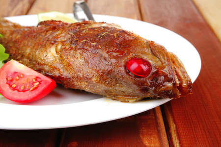 main portion of two grilled fish served on plate with tomatoes and spicesの写真素材