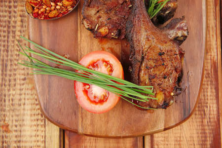 meat on wooden plate : roast ribs on wood with tomatoes chives and dry spices over wooden table