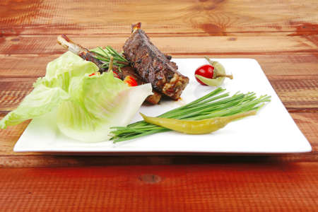 meat savory on wooden table: roast ribs on white plate with peppers lettuce tomato and chivesの写真素材