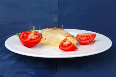 food : vegetable casserole triangle on white plate with pepper and tomatoes on blue tableの写真素材
