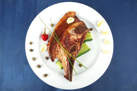 fresh grilled beef meat fillet on white plate with tomatoes and capers on blue wooden tableの写真素材