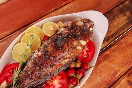 main course: whole fryed sunfish on wooden table with lemons and peppersの写真素材