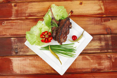 meat plate over wooden table: grilled ribs on white plate with red hot peppers, tomatoes and chivesの写真素材