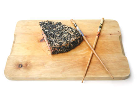 tuna piece roasted with black sesame over wooden board with chopsticks over white backgroundの写真素材