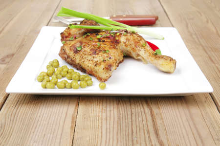 roast meat : roasted chicken legs garnished with green peas , peppers , and garlic on white plates...