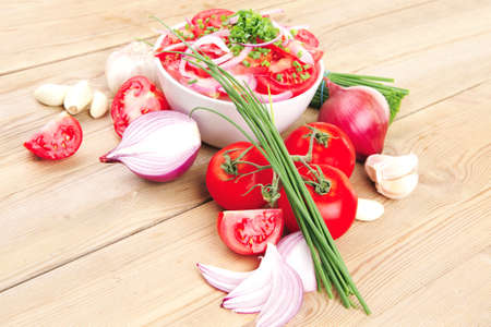 vegetable food : fresh tomato salad in white bowl with bundle of chives and raw tomatoes on twig over wooden tableの写真素材