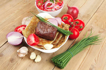 meat food : roasted fillet mignon on bread in white bowl garnished with tomatoes salad on wooden tableの写真素材