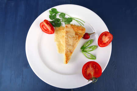 food : vegetable casserole piece over white plate served with parsley and tomatoes on blue tableの写真素材