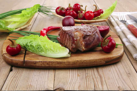 meat savory : beef grilled and garnished with green lettuce and red chili hot pepper on wooden table with cutleryの写真素材