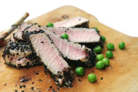 tuna slices roasted with black sesame and green peas on wooden plate with chopsticks over whiteの写真素材