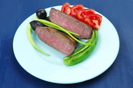 meat savory : grilled beef fillet mignon served on blue plate over blue wooden table with chili pepper and tomatoesの写真素材