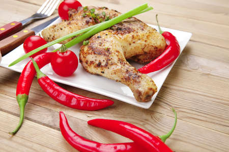 meat : chicken quarters garnished with red hot peppers on white plates over wooden tableの写真素材