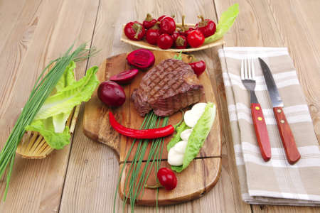 meat savory : beef grilled and garnished with green lettuce and red chili hot pepper on wooden table with cutleryの写真素材