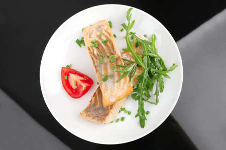 savory sea fish : roasted salmon fillet garnished with green rocket leaves and tomatoes on black dish isolated over black backgroundの写真素材