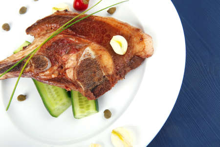 fresh hot roasted beef meat bone steak on ceramic dish with red hot pepper and capers on blue wooden tableの写真素材