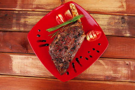 savory plate : roasted meat shoulder on red plate with chives and tomato over wooden tableの写真素材