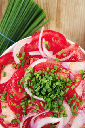 healthy appetizer : fresh tomato salad in white bowl with bunch of chives and raw tomatoes on twig , violet onion, over wooden tableの写真素材