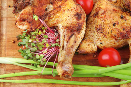 roast meat : chicken legs garnished with green sprouts and peppers on wooden plate isolated over white backgroundの写真素材