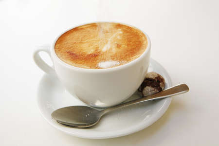 sweet drink : small white cup of cappuccino coffee on light background with spoonの写真素材