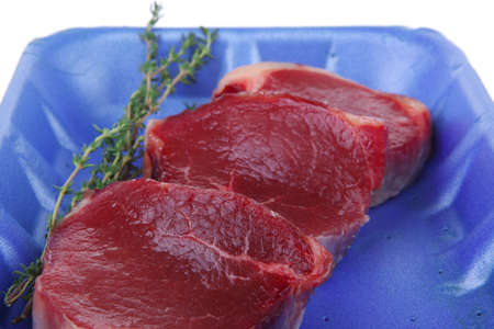 uncooked raw beef fillet with thyme twig on blue tray isolated over white background