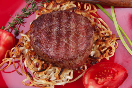 grilled beef fillet medallions on noodles with red hot chili pepper on red plate over wood tableの写真素材