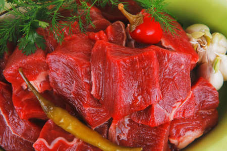 uncooked fresh beef meat chunks on ceramic bowls with vegetables and red peppers isolated over white...