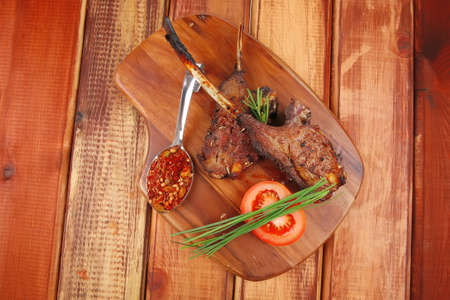 meat savory on wooden plate: roast ribs with peppers tomato and dry spices over wooden table