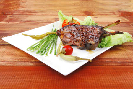 savory plate over wooden table: grilled ribs on white plate with chives, red hot peppers lettuce